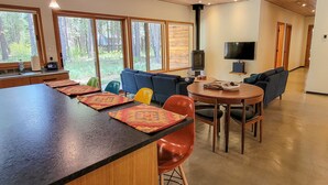 A modern kitchen with a long counter, dining area with chairs, sofas, and a TV. - Petrichor - Mazama Modern Cabin (Mazama)
