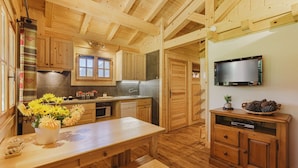 A wooden interior with a kitchen area, wooden cabinets, a dining table with benches, and a flat-screen TV mounted on the wall.