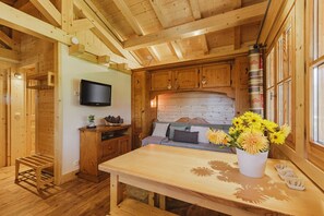 A wooden interior with a dining table, a TV mounted on the wall, and a window with curtains.