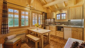 A cozy wooden cabin with a dining area, kitchen, and large windows.