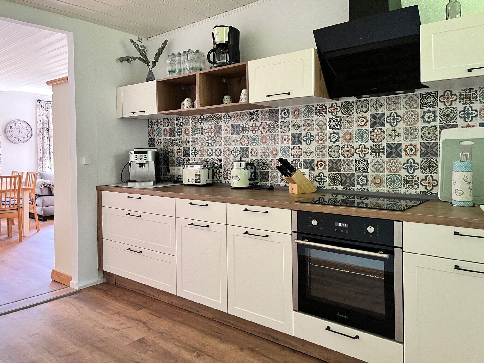 Et moderne køkken med lyse skabe, indbygget ovn, kaffemaskine og et mønstret backsplash.