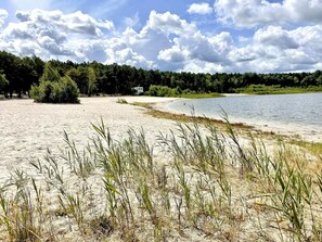 Una playa arenosa con un lago, árboles y una estructura pequeña al fondo.