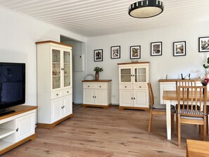 Un salon spacieux équipé d’un téléviseur, de meubles en bois, d’un coin repas avec des chaises et d’un luminaire au plafond.