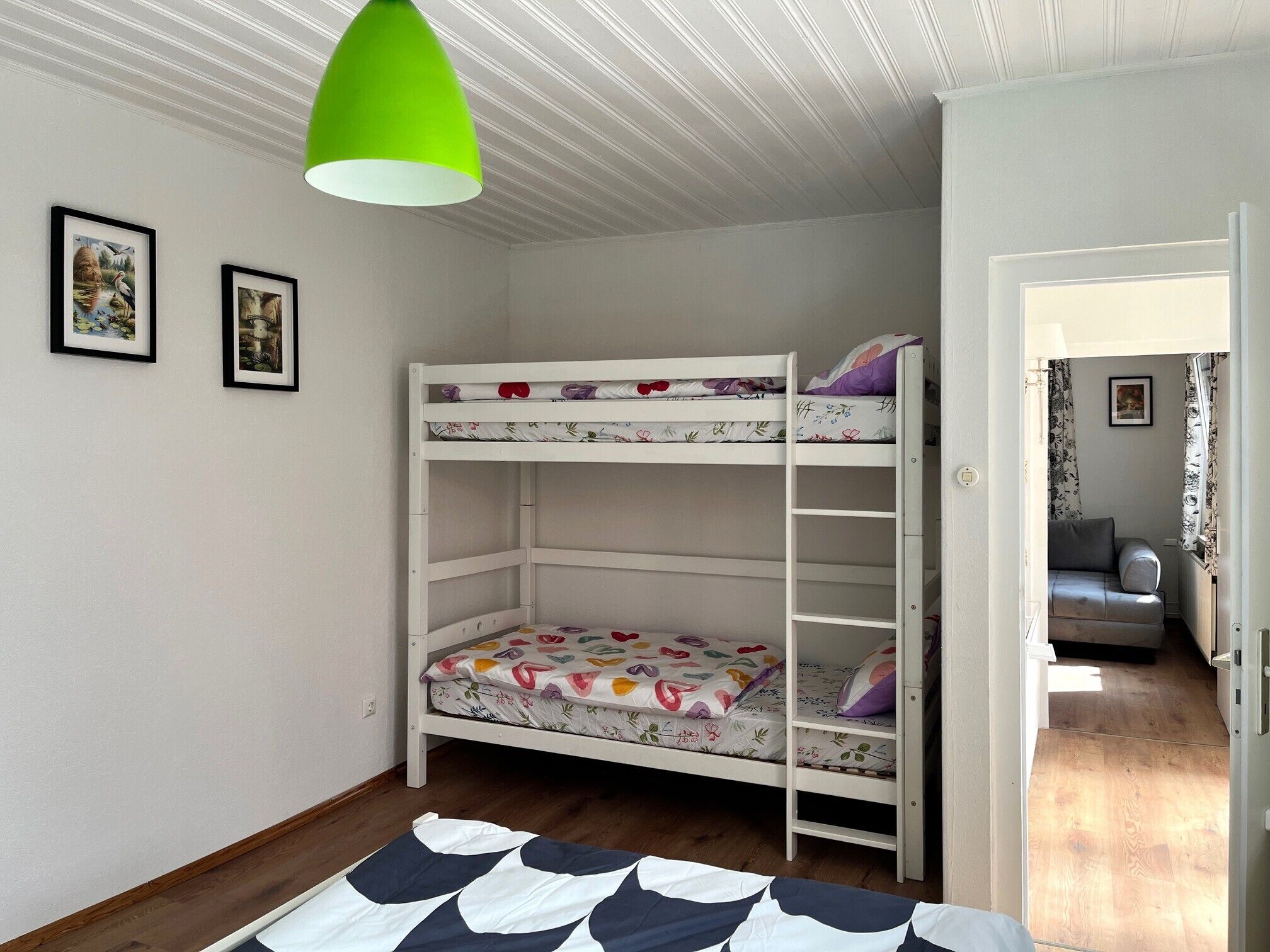 A bunk bed room with a green pendant light, wooden flooring, and a door leading to another room.