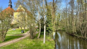 Un sentier qui longe la rivière, avec une église, des arbres et une zone herbeuse.