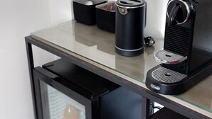 A modern kitchen with a glass-top table, a coffee machine, a kettle, and a small refrigerator. - Süßes Gästehäuschen in 1A Lage (Bochum)