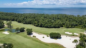 Un campo de golf con búnkeres de arena, un estanque y un bosque denso al fondo.