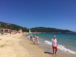 A beach with people walking along the shore, a clear blue sky, and buildings in the background.