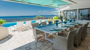 A dining area with a view of the sea, outdoor seating, and a pool.