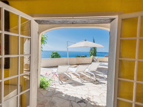 A patio with stone flooring, white lounge chairs, and a white umbrella.