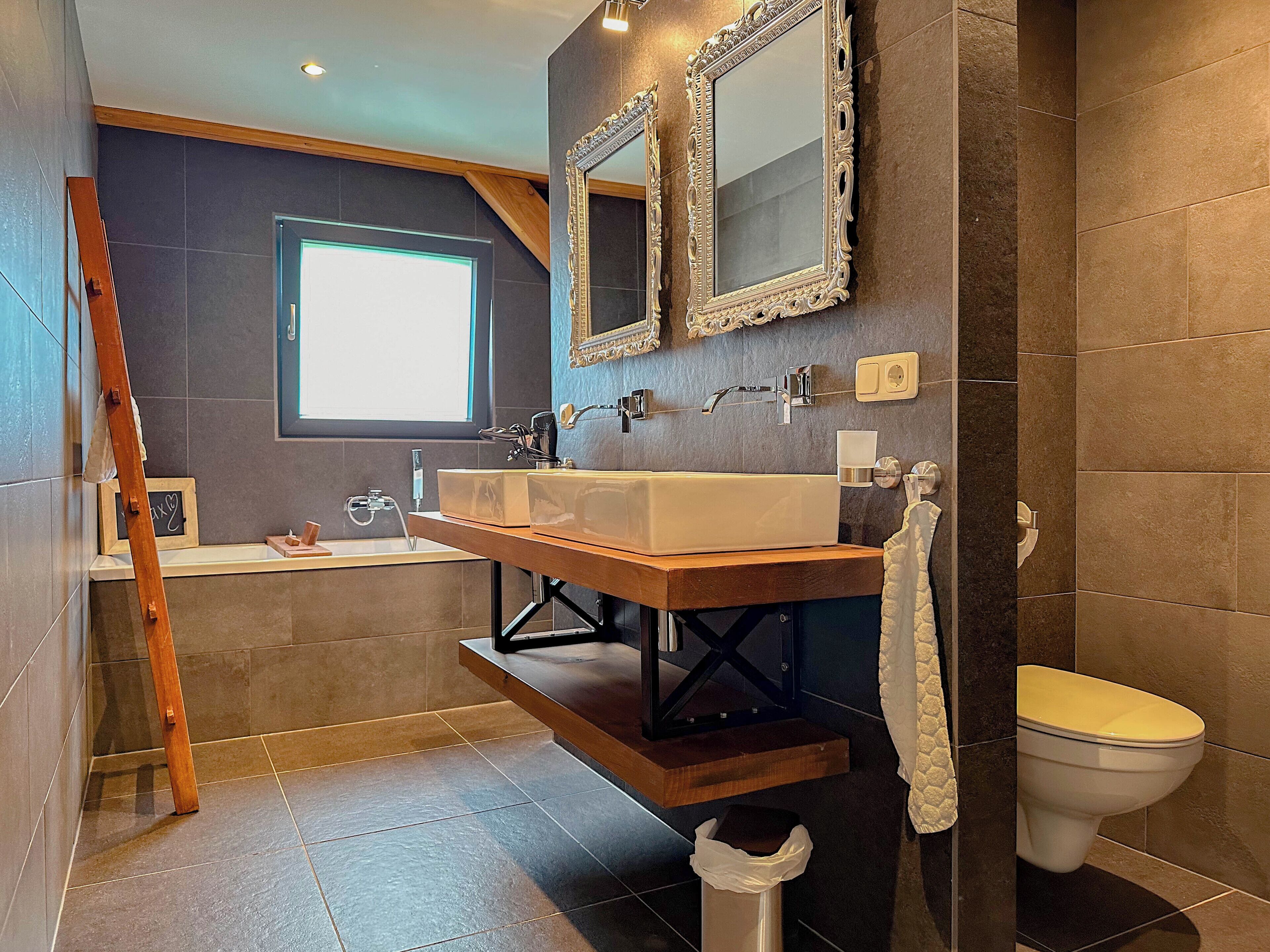 A modern bathroom with a wooden vanity, two mirrors, a bathtub, and a toilet.
