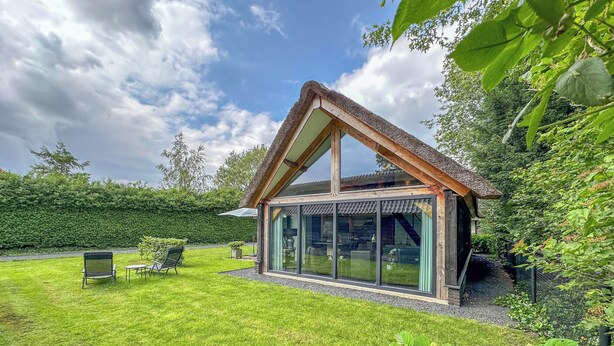 A modern house with a thatched roof, large glass windows, and a well-maintained lawn. - Tastefully decorated country villa (Alphen)