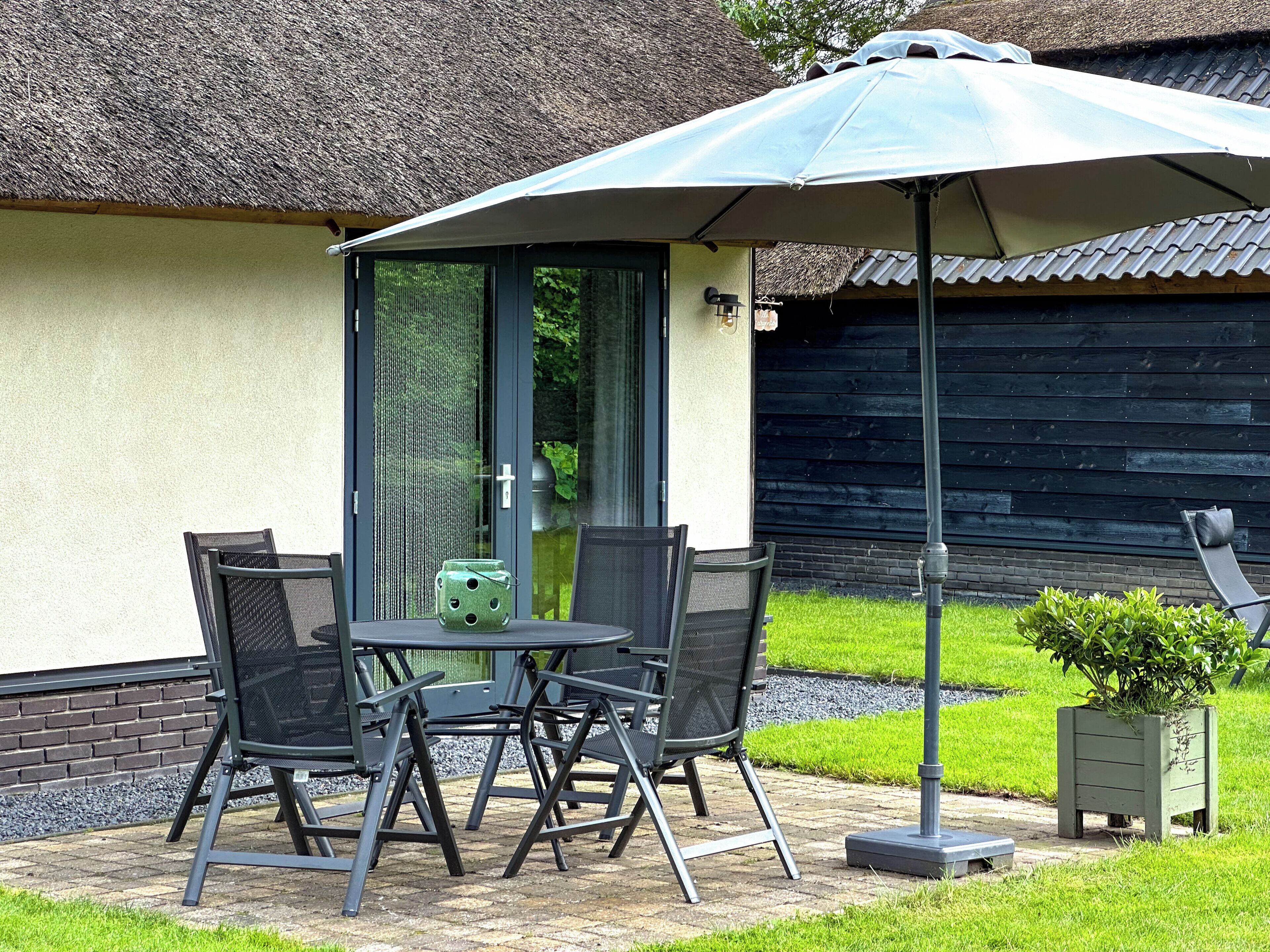 An outdoor patio with a table and chairs, a thatched-roof building, and a wooden fence in the background.