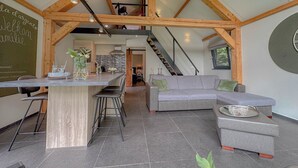 A modern interior with a kitchen island, grey sofa, and a staircase leading to an upper level. - Tastefully decorated country villa (Alphen)
