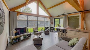 A spacious living area with a large sofa, a TV, and a dining table with bar stools. - Tastefully decorated country villa (Alphen)