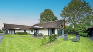 A modern house with a thatched roof, a patio with outdoor furniture, and a well-maintained lawn. - Tastefully decorated country villa (Alphen)