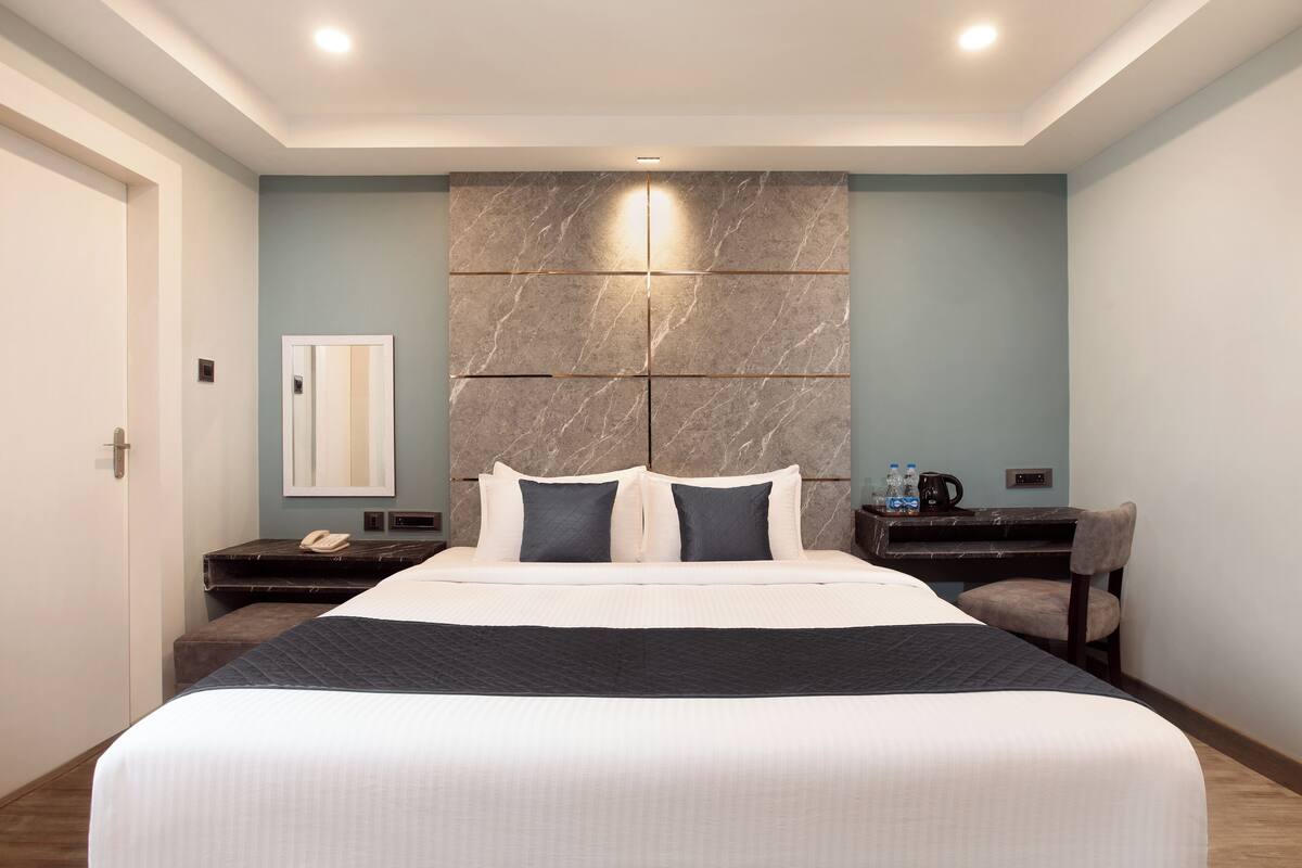 Una habitació d'hotel moderna amb un llit gran, una taula de treball amb una cadira, un mirall i una tauleta de nit.