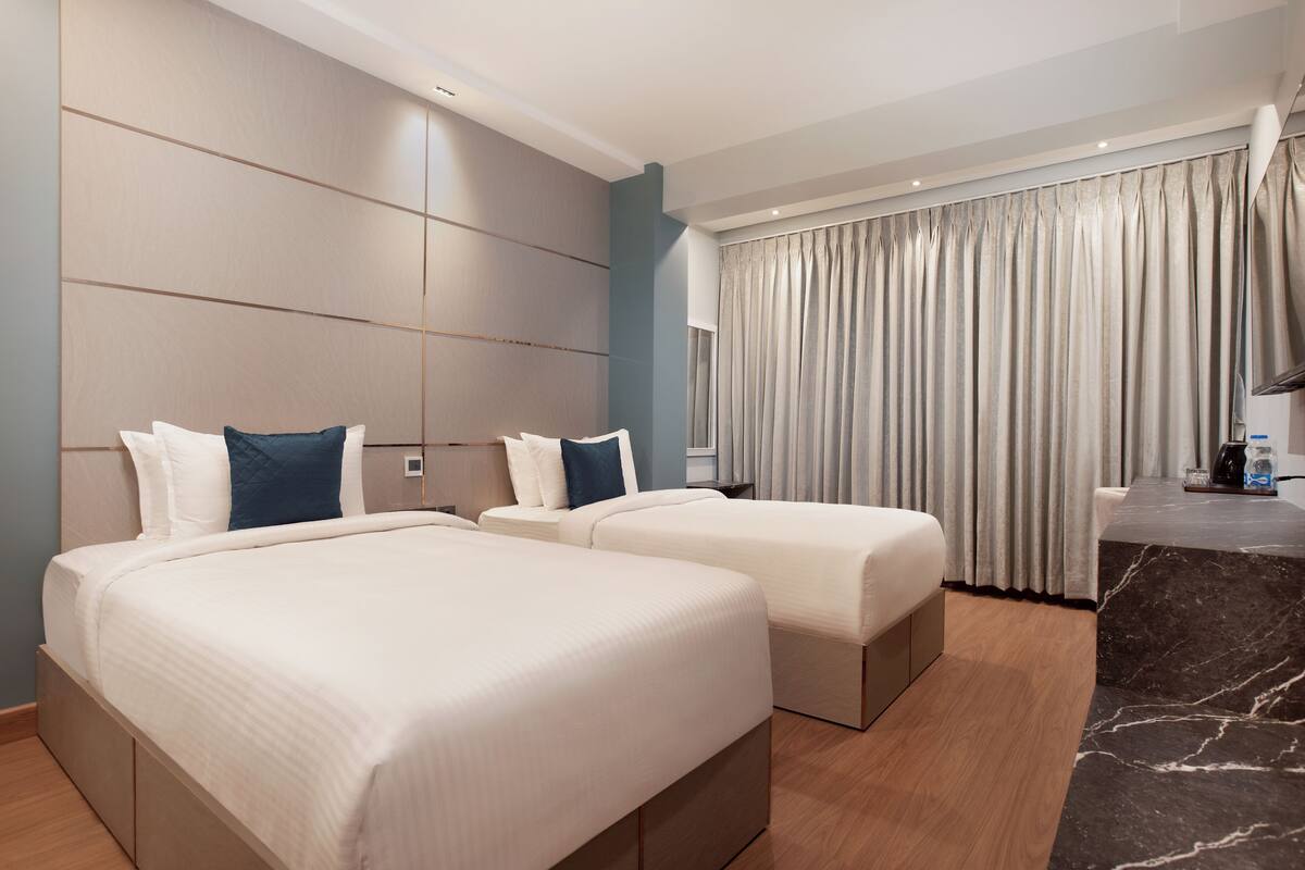 Habitació d'hotel amb dos llits, escriptori de marbre i una finestra gran amb cortines.