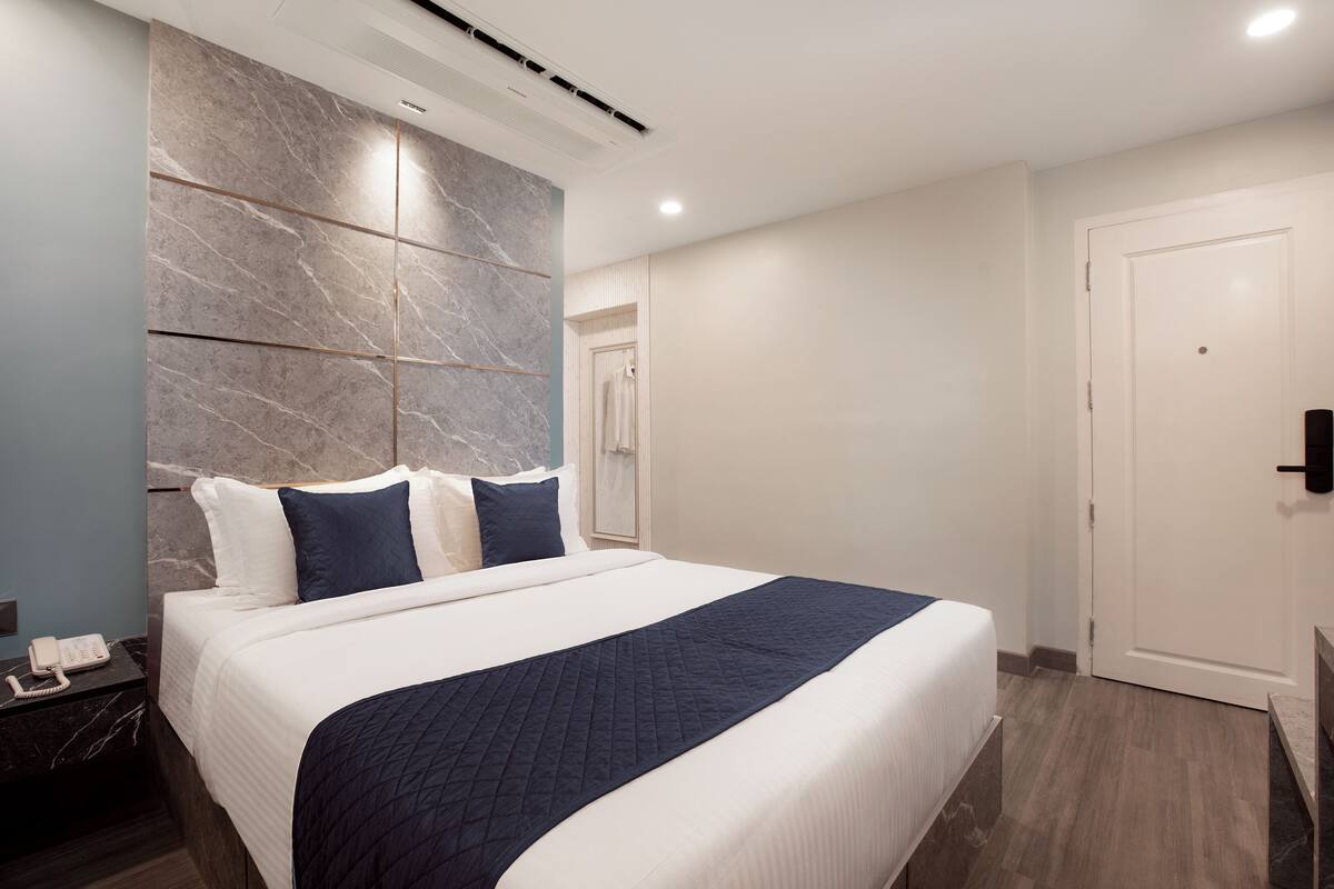Habitació d'hotel moderna amb un llit gran, una paret decorativa de marbre, un telèfon al costat del llit i una porta a la dreta.