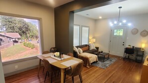 A spacious living room with a dining area, wooden flooring, a sofa, a coffee table, and a TV in the background.