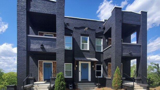 A modern two-story townhouse with a dark brick exterior, multiple windows, and a front entrance with steps.