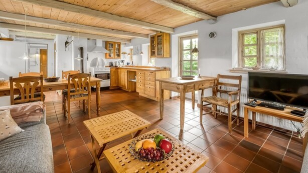 Une cuisine spacieuse avec des meubles en bois, un coin repas comprenant une table et des chaises, un téléviseur et un panier de fruits posé sur une petite table.