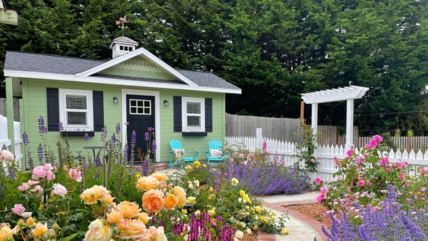 A green house with a porch, surrounded by a garden with various flowers and a white fence. - 🌹Cutest Garden Cottage🌹Lopez Village-Walk to Beach, Dining, Brewery, Farm Mkt
 (Lopez Island)