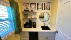 A compact kitchen with a microwave, coffee maker, and sink. There are framed pictures on the wall and a window with blinds. - 🌹Cutest Garden Cottage🌹Lopez Village-Walk to Beach, Dining, Brewery, Farm Mkt
 (Lopez Island)