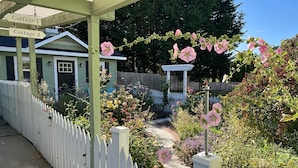 A garden with a white picket fence, a pathway, and a gazebo. There are signs indicating 'Cottage 1' and 'Cottage 2'. - 🌹Cutest Garden Cottage🌹Lopez Village-Walk to Beach, Dining, Brewery, Farm Mkt
 (Lopez Island)