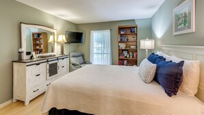 Une chambre à coucher avec un grand lit, une commode, une chaise, une bibliothèque, un téléviseur et une fenêtre avec des rideaux.
