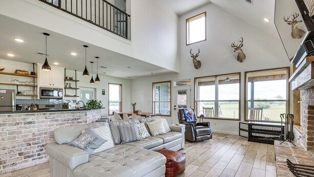 A spacious living area with a large white leather sofa, a brick accent wall, and a fireplace. - Modern Bryan Farmhouse on 1 Acre w/ Hot Tub! (Bryan)