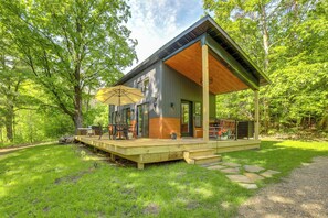 Ein modernes Haus mit einer Holzterrasse, Gartenmöbeln und einem großen Sonnenschirm.