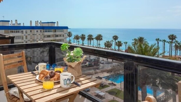 Un balcón con alimentos para el desayuno, vista al océano y un edificio al fondo.