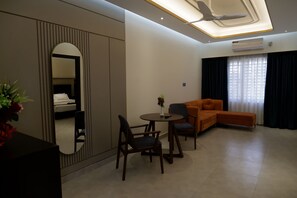 Una habitación de hotel moderna con sofá, una mesa de comedor con sillas, un espejo y un ventilador de techo.