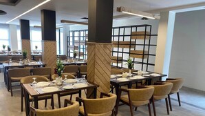 Un comedor moderno con mesas y sillas de madera, dispuesto en un espacio amplio con ventanas grandes que dejan entrar luz natural.