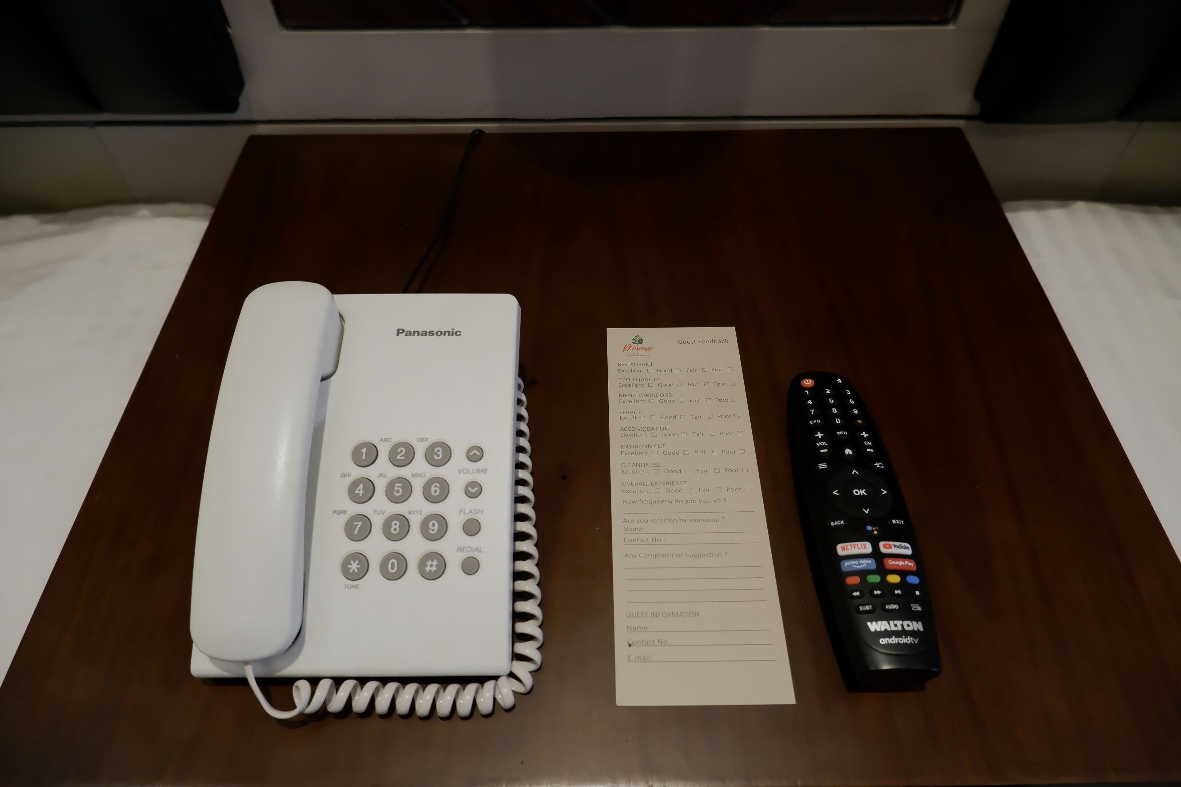 A Panasonic landline phone, a guest feedback form, and a remote control on a wooden table.