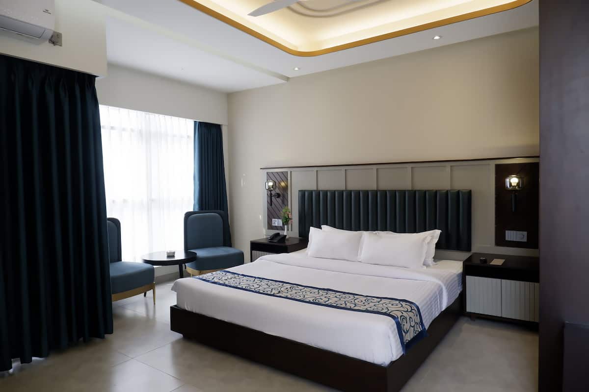 Moderni hotellihuone, jossa on suuri sänky, työpöytä, tuoli ja ikkuna, jossa on verhot.