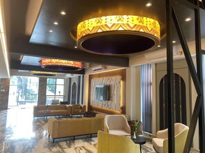 A modern lobby with a marble floor, a sofa set, a TV mounted on the wall, and decorative lighting fixtures.