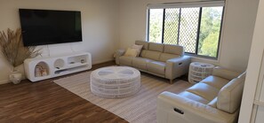 A living room with a sofa, ottoman, and TV. - Starfish Beach House (Agnes Water)