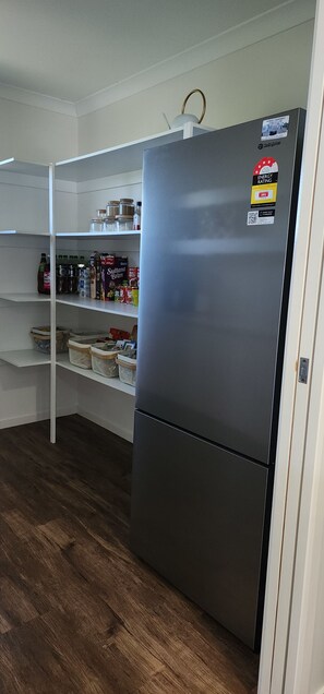 A kitchen with a stainless steel refrigerator, white shelving, and wooden flooring. - Starfish Beach House (Agnes Water)