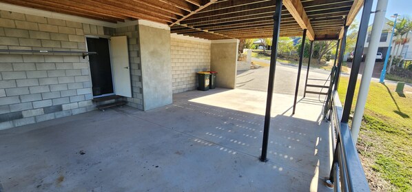 A covered outdoor area with a concrete floor, a door, and a trash bin. - Starfish Beach House (Agnes Water)