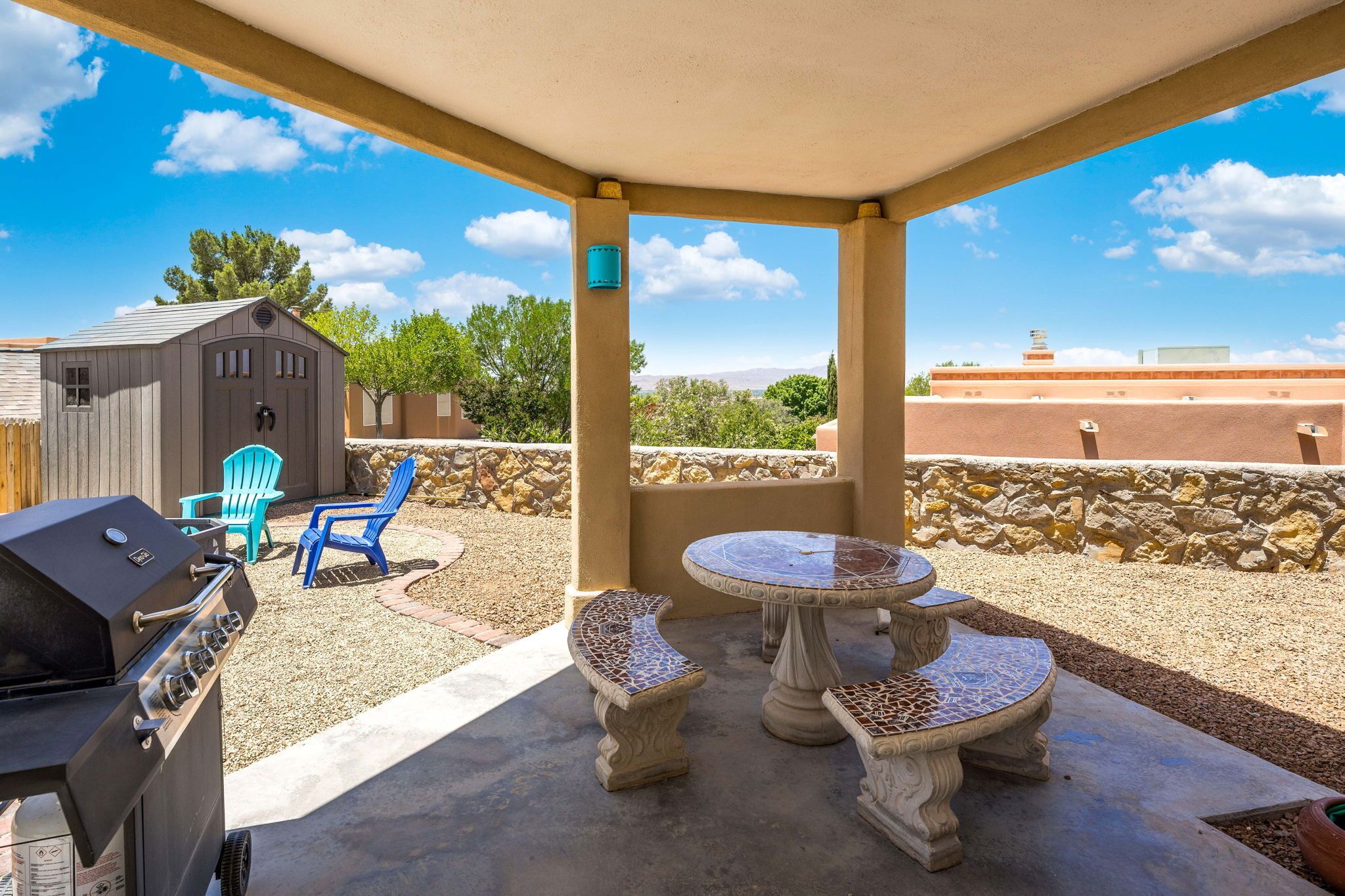 Un patio al aire libre con una parrilla, dos sillas azules y una mesa de mosaico.
