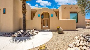 A stucco building with a central archway, a palm tree, and a cactus in the foreground. - Luxury Desert Pool Oasis Home (Las Cruces)