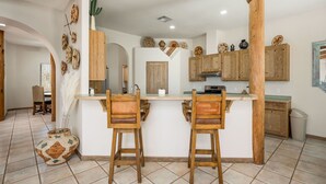 A kitchen with a central island, wooden bar stools, and a rustic decor. - Luxury Desert Pool Oasis Home (Las Cruces)
