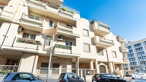 A multi-story residential building with balconies, a parking area, and a clear blue sky. - GuestHost - Cozy apartment of approximately 28 sqm, ideal for 2 people, located on the ground floor of a building WITHOUT a lift (NOT suitable for disabled people).The apartment is located in a central neighborhood, served by all the main services: bars, (Cagliari)