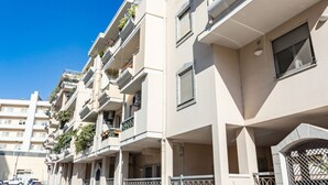 A multi-story residential building with balconies, a gated entrance, and a clear blue sky. - GuestHost - Cozy apartment of approximately 28 sqm, ideal for 2 people, located on the ground floor of a building WITHOUT a lift (NOT suitable for disabled people).The apartment is located in a central neighborhood, served by all the main services: bars, (Cagliari)