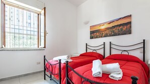 A hotel room with two single beds, a large window, a painting on the wall, and a tiled floor. - GuestHost - Cozy apartment of approximately 28 sqm, ideal for 2 people, located on the ground floor of a building WITHOUT a lift (NOT suitable for disabled people).The apartment is located in a central neighborhood, served by all the main services: bars, (Cagliari)