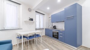 A compact kitchen with a dining area, a clock on the wall, and a window with curtains. - Moby Dick Central Flat x3 (Genova)