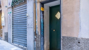 A closed metal shutter door, a green door with a diamond-shaped window, and a wall with graffiti. - Moby Dick Central Flat x3 (Genova)