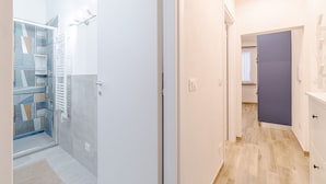 A hallway with a glass door leading to a bathroom, a white door, and a blue door. - Moby Dick Central Flat x3 (Genova)